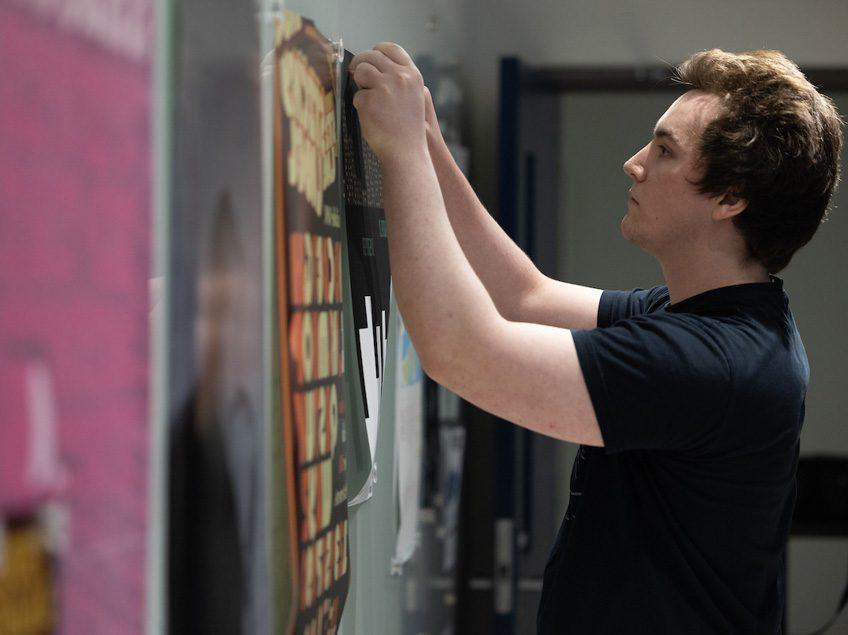 A student hangs a large printed poster.